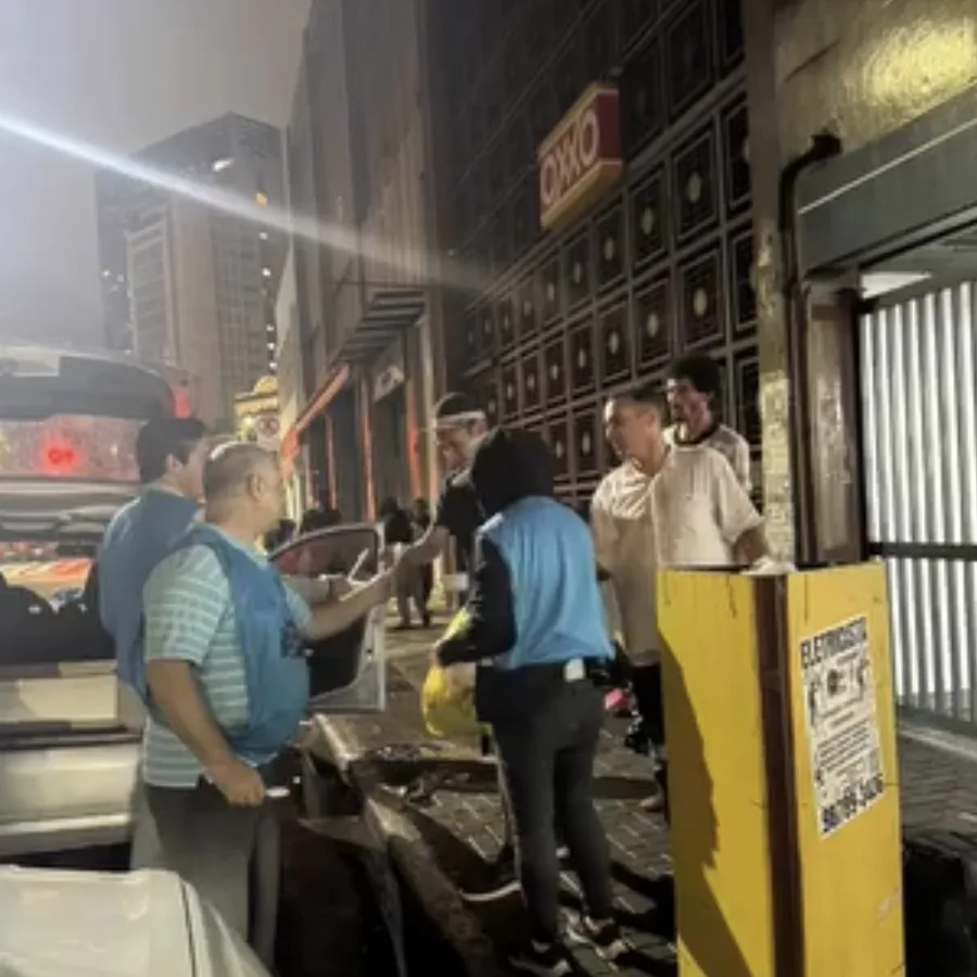 Voluntários de colete azul do Cambuci Solidário na rua, à noite